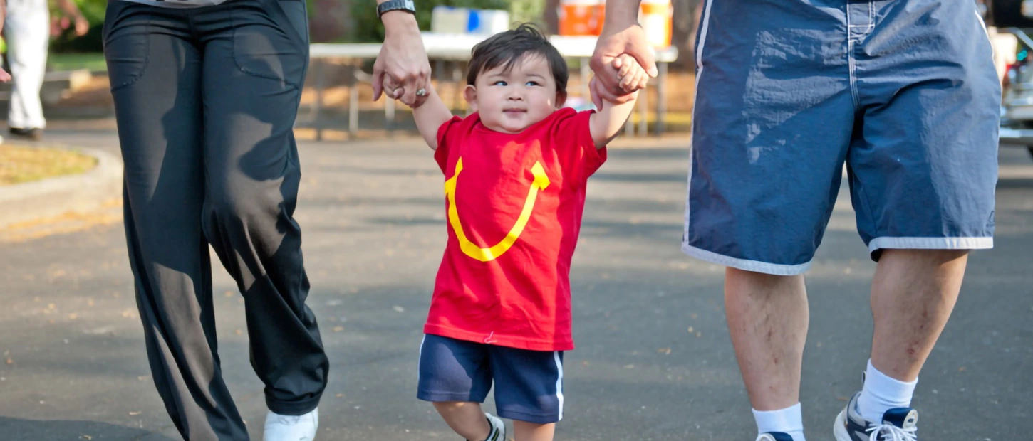 young participant wearing a red McDonalds shirt in a charity run with his hands being held on either side by his parents