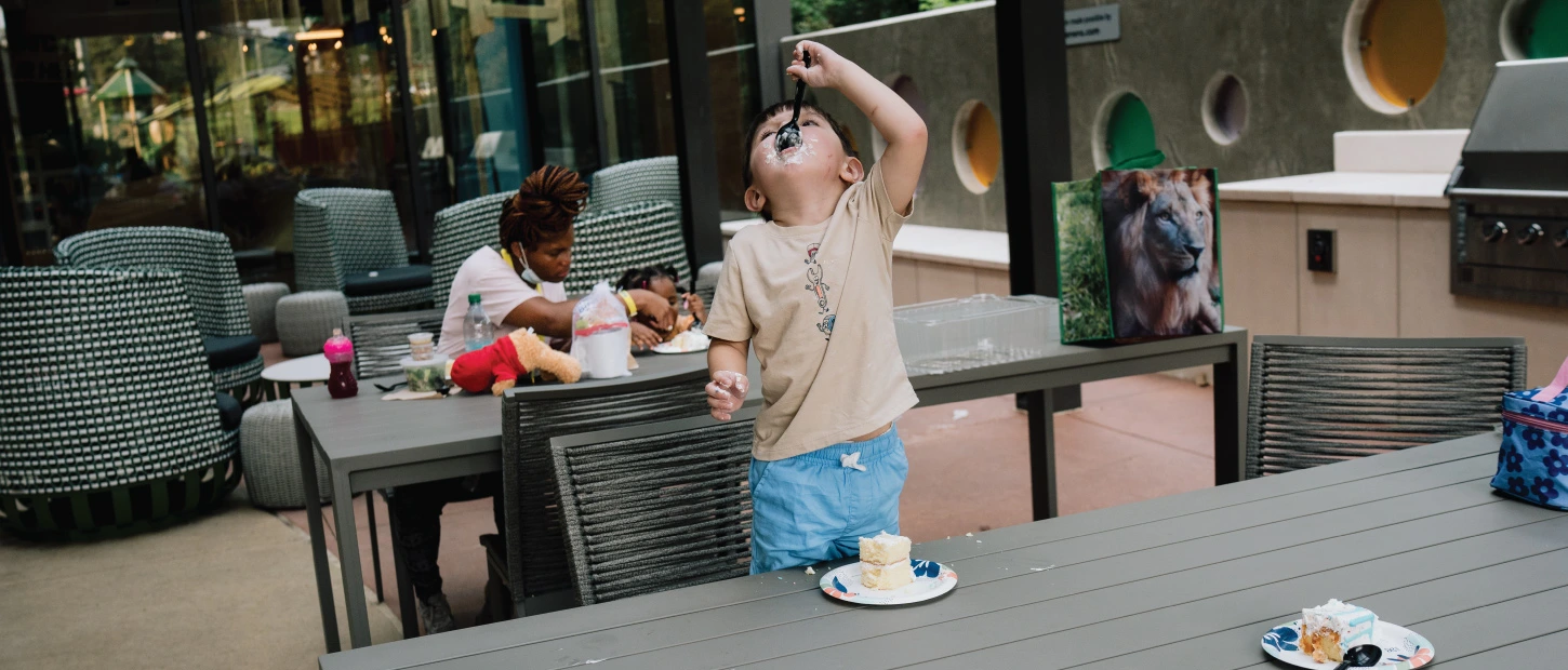 young boy excitedly eating a slice of cake outdoors at picnic table