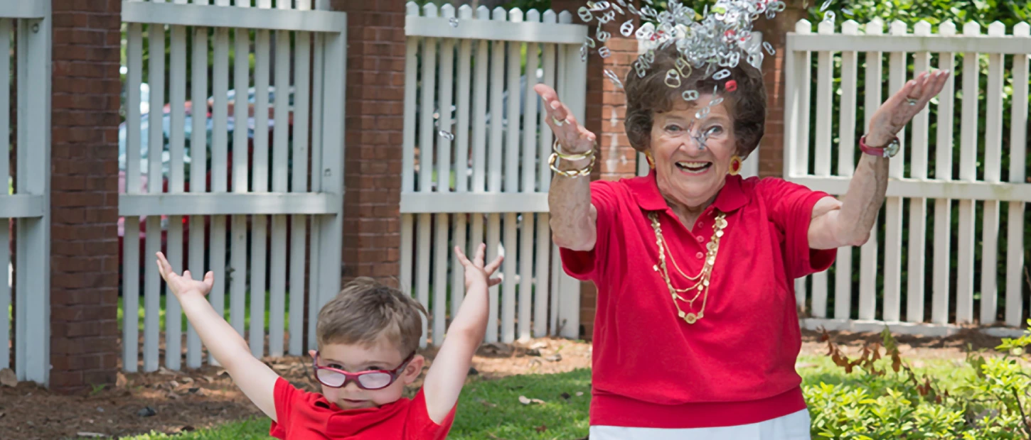 Grandmother and grandchild both in red shirts excitedly throwing up handfuls of pop tabs into the air