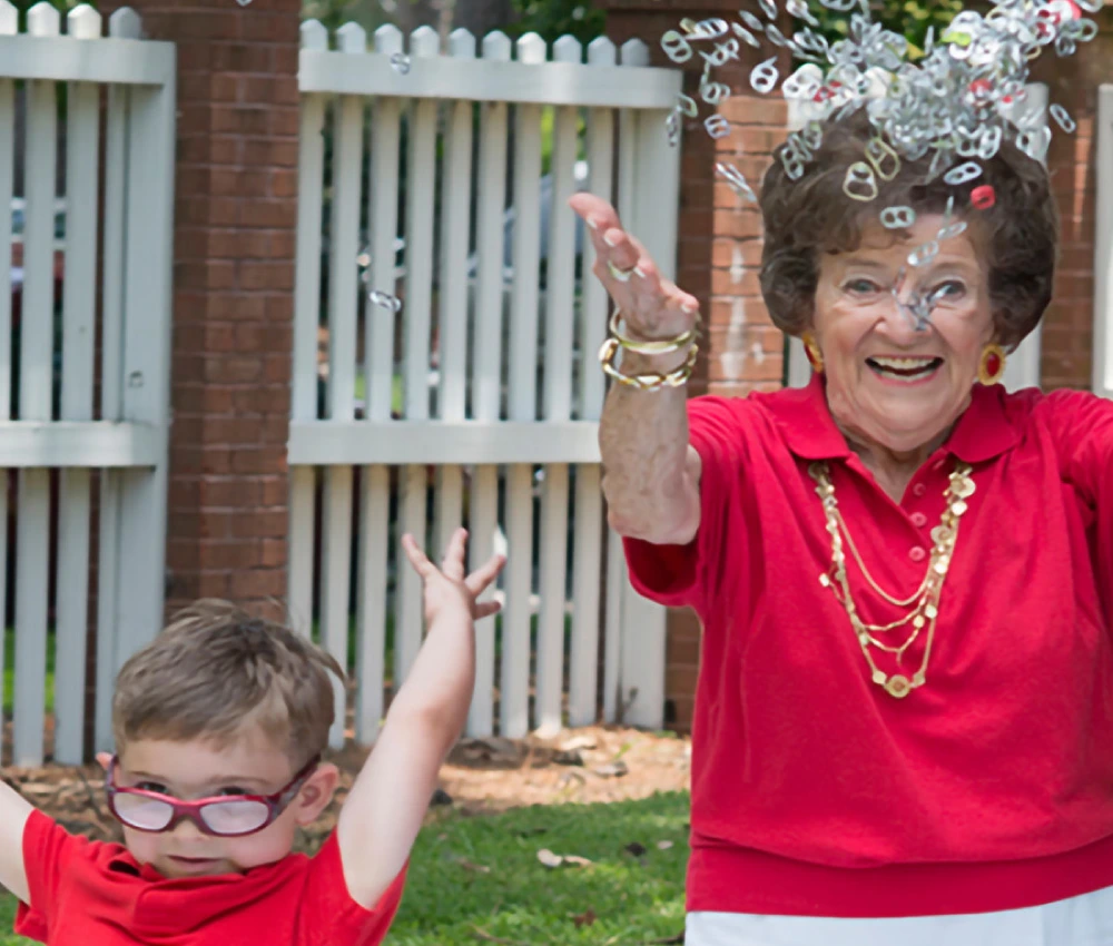 Grandmother and grandchild both in red shirts excitedly throwing up handfuls of pop tabs into the air